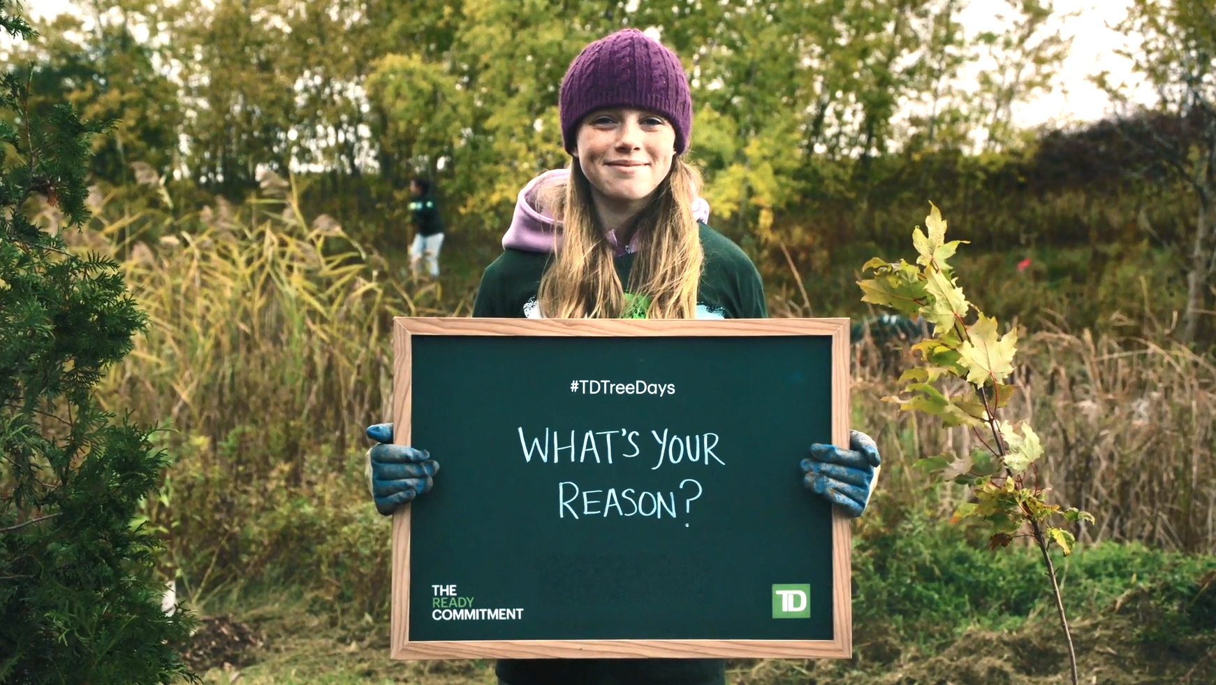 A volunteer holding sign that says: #TD Tree Days. What's Your Reason? The Ready Commitment